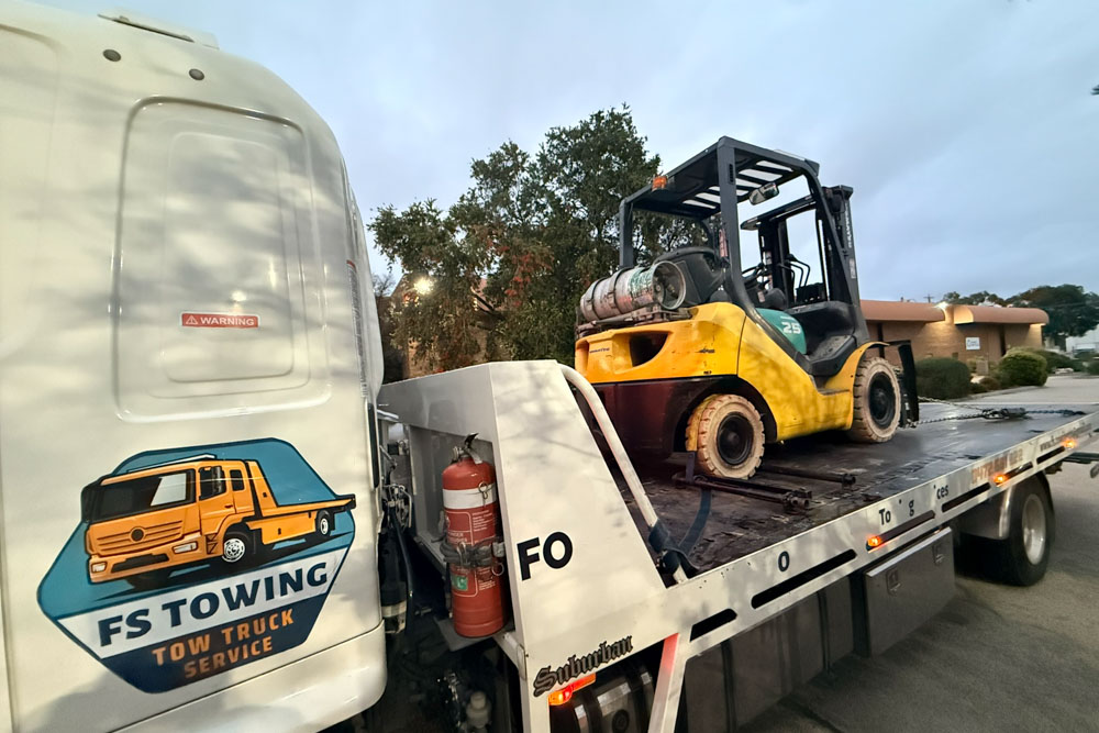 Transporting forklift on flatbed tow truck